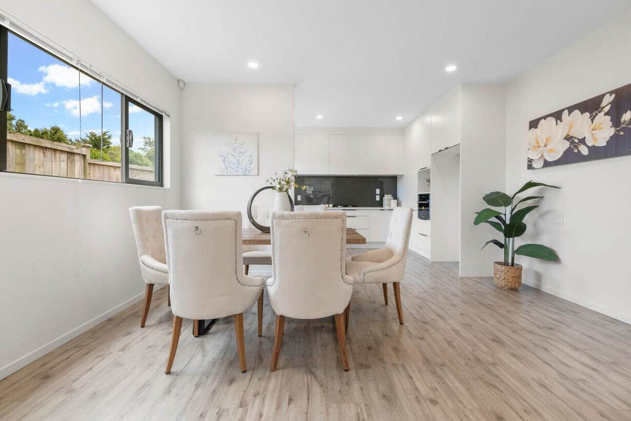 Dining table and chairs in an open living space looking through to the kitchen, Albany Village