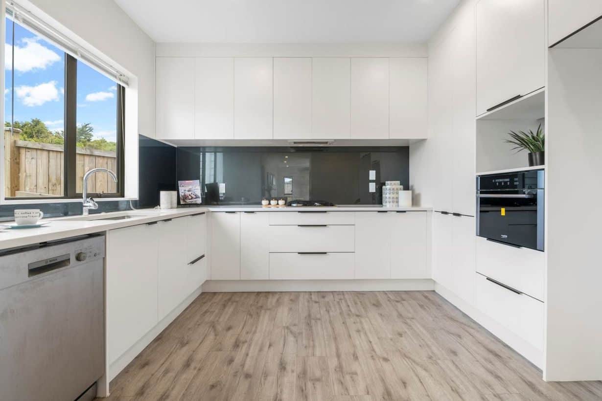 U-shaped white kitchen with a dark glass splashback, wall oven and dishwasher, Albany Village