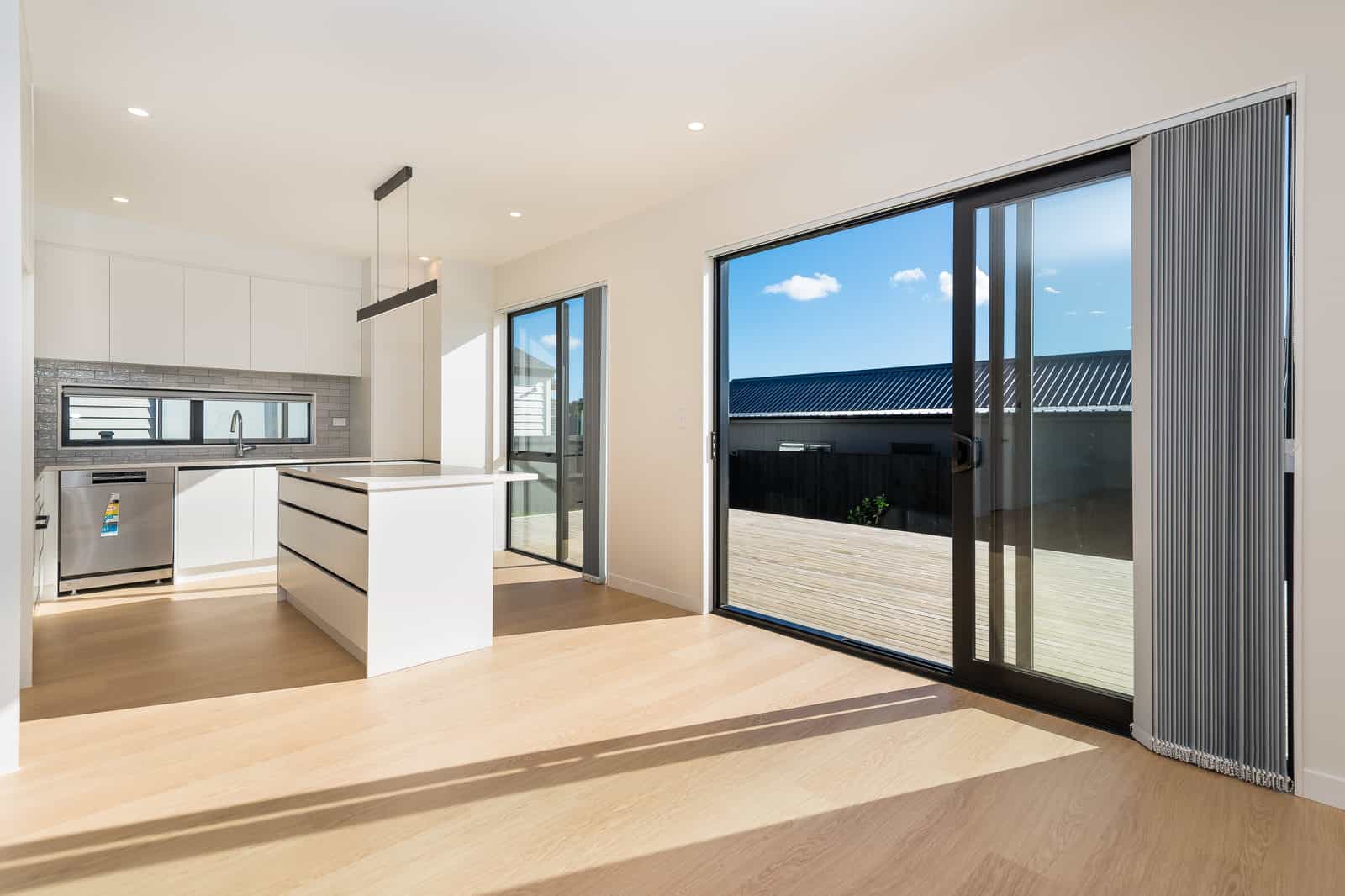 Kitchen with an island opening through a wide slider onto a timber deck, Orewa