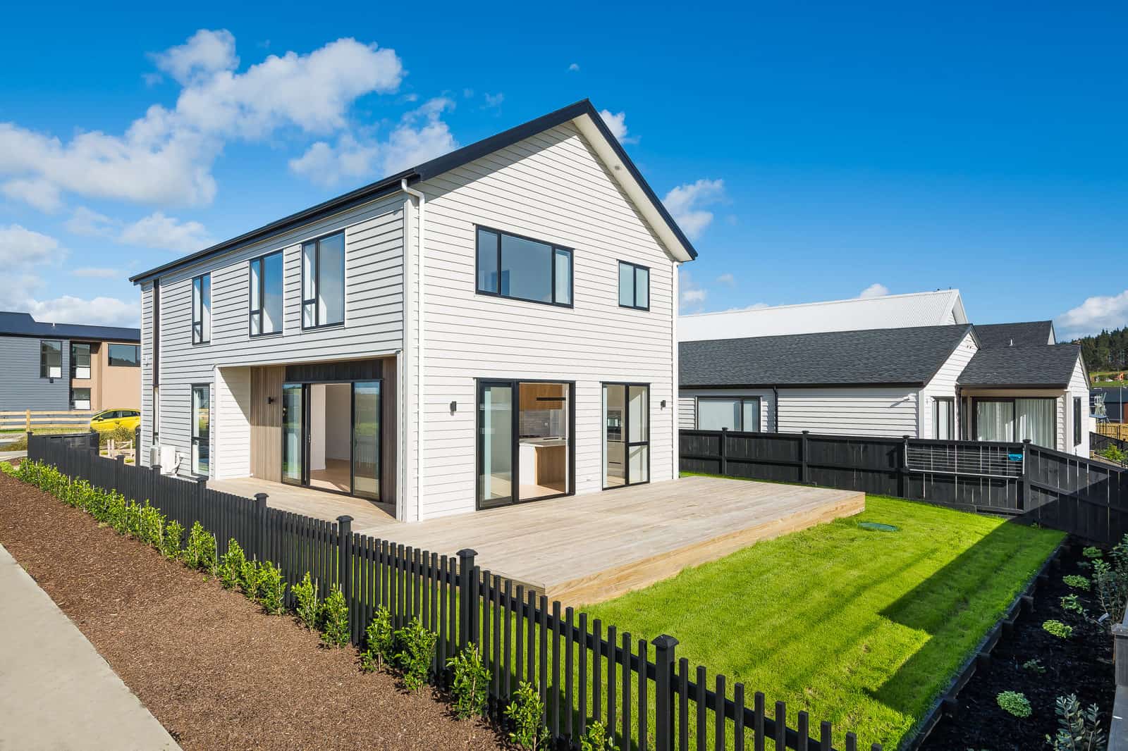 Two-storey weatherboard house with a gabled roof behind a picket fence, Orewa