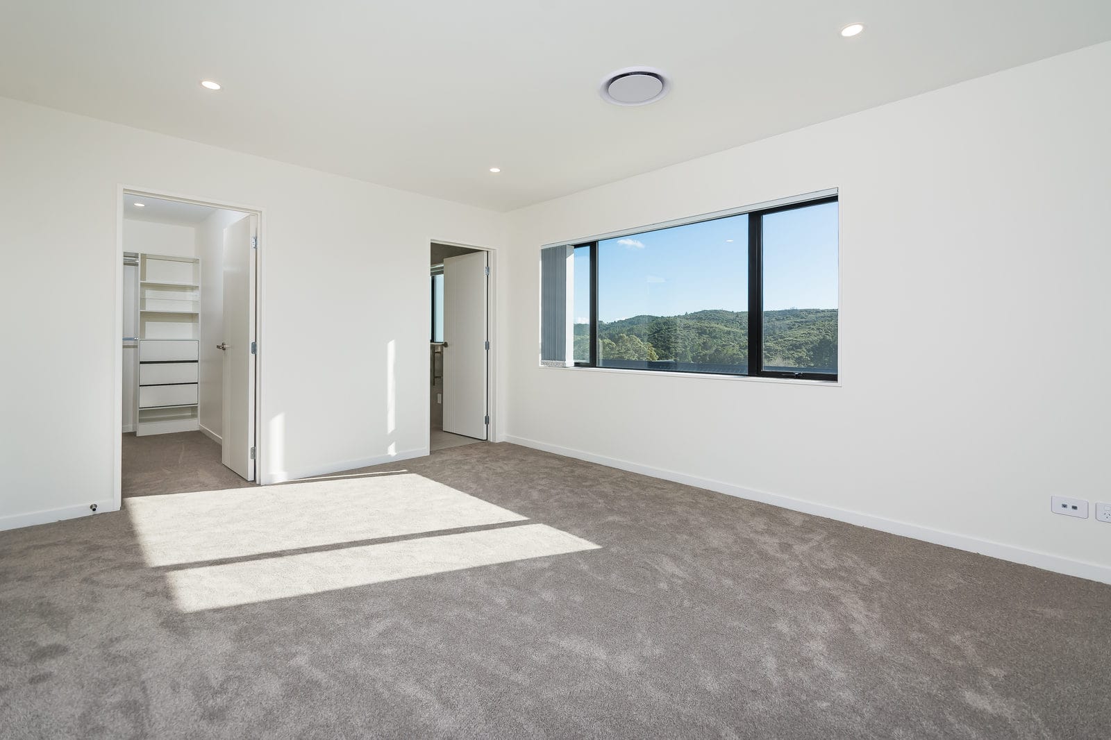 Empty carpeted bedroom with a wide window and a walk-in wardrobe, Orewa