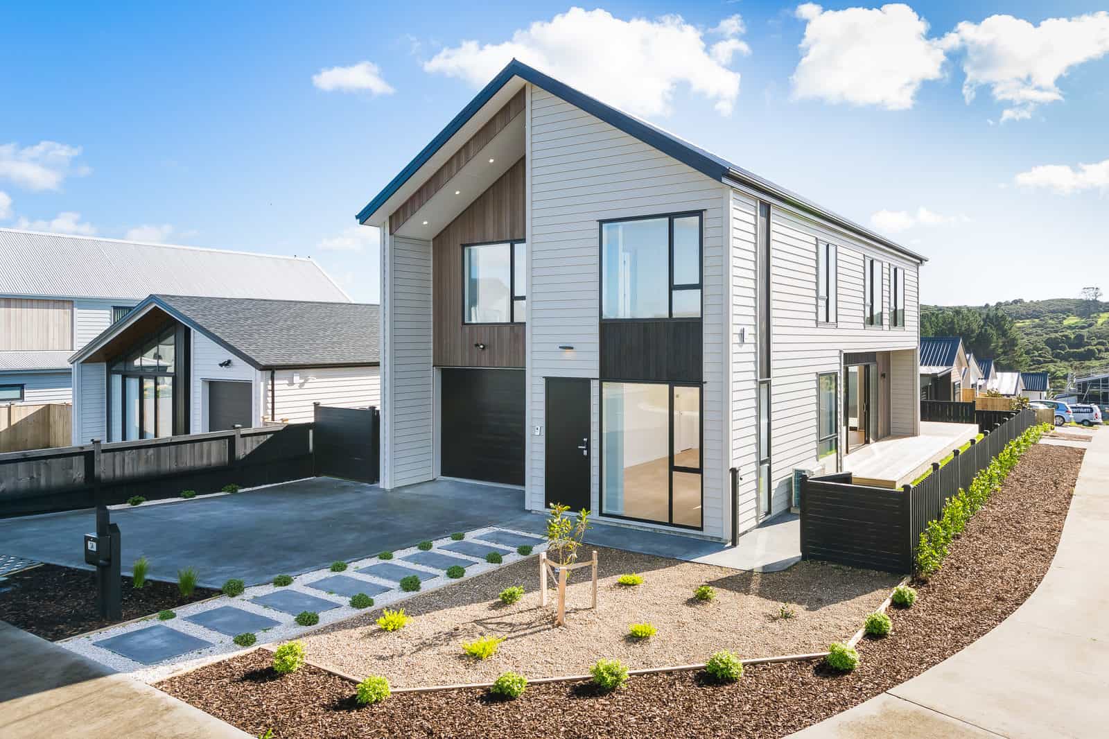 Two-storey house in dark and light cladding with a stepping-stone path and new planting, Orewa