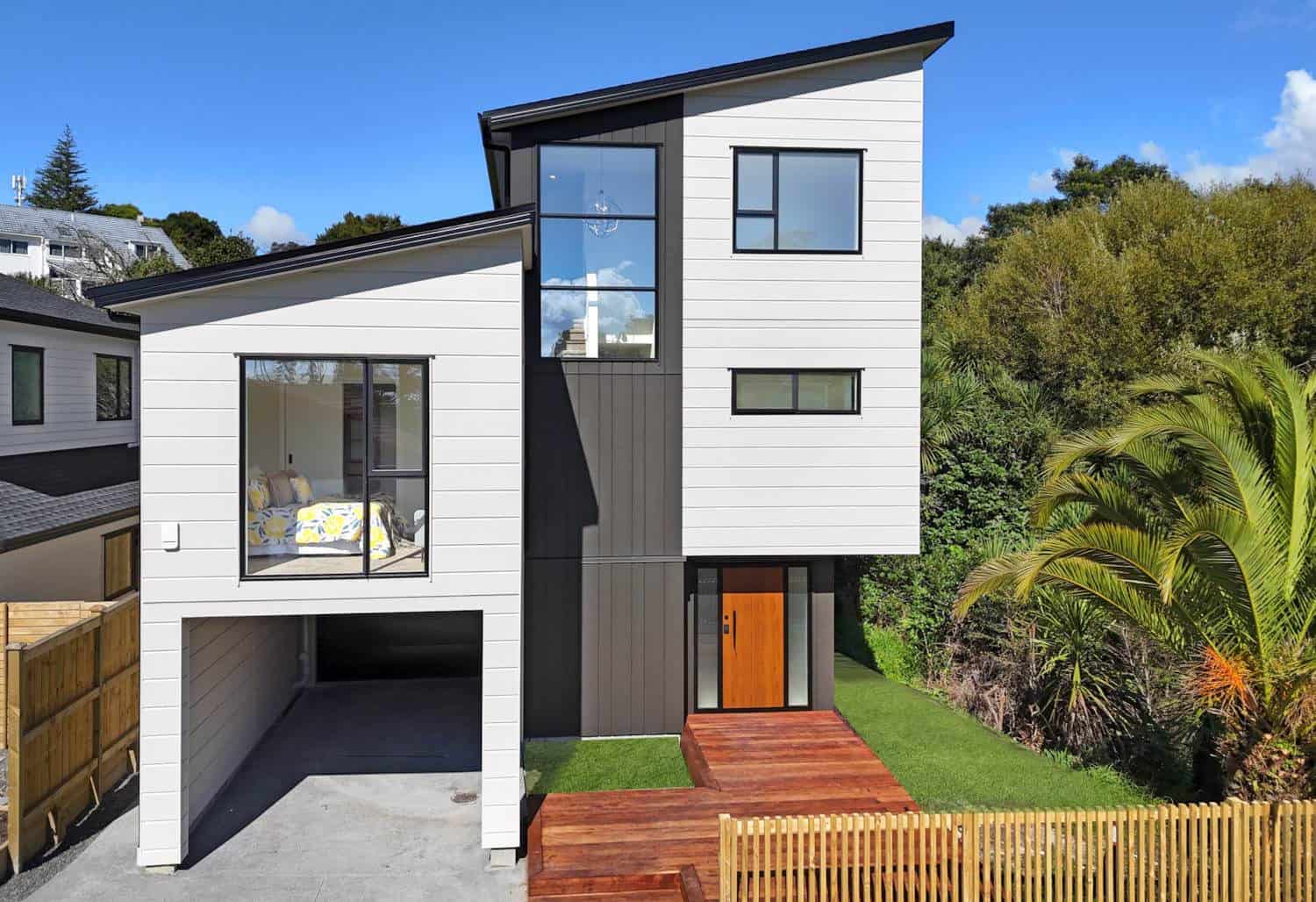 Three-level house in white and dark cladding on a bush-edged site, Browns Bay