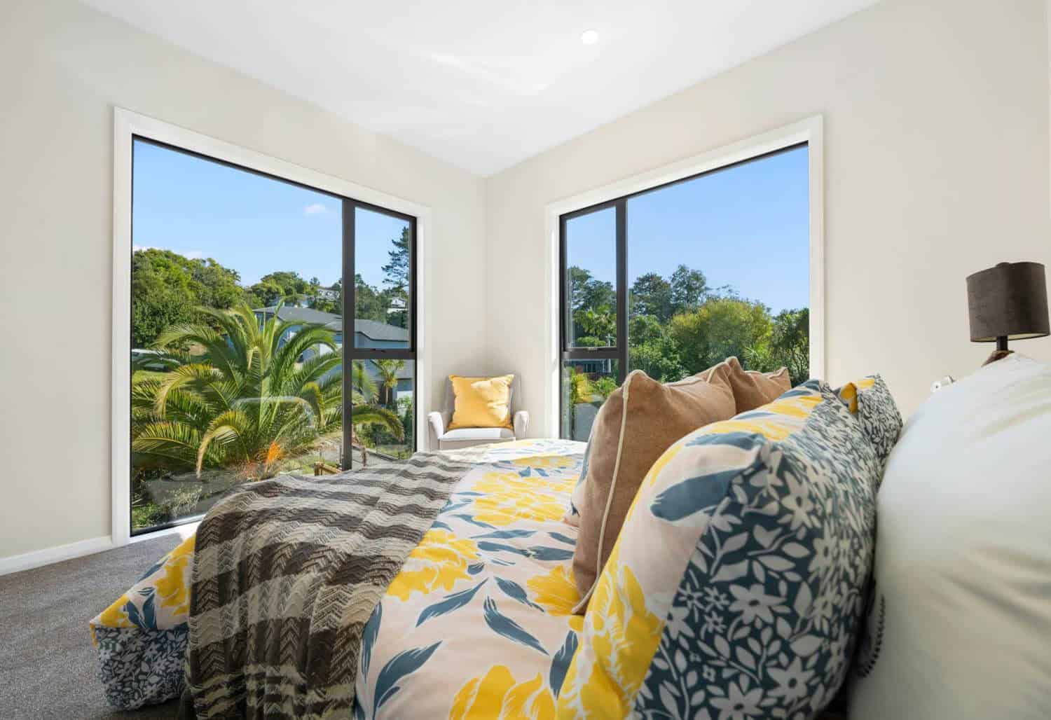 Bedroom with two tall windows looking into palms and bush, Browns Bay