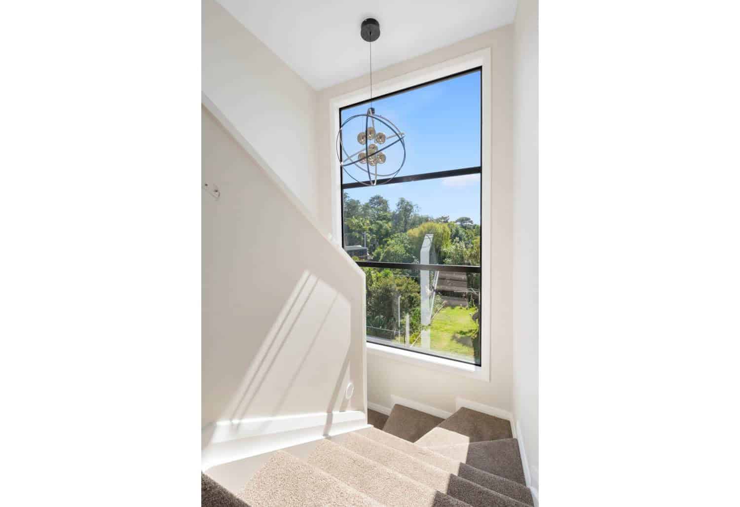 Stairwell lit by a tall window looking into bush, Browns Bay