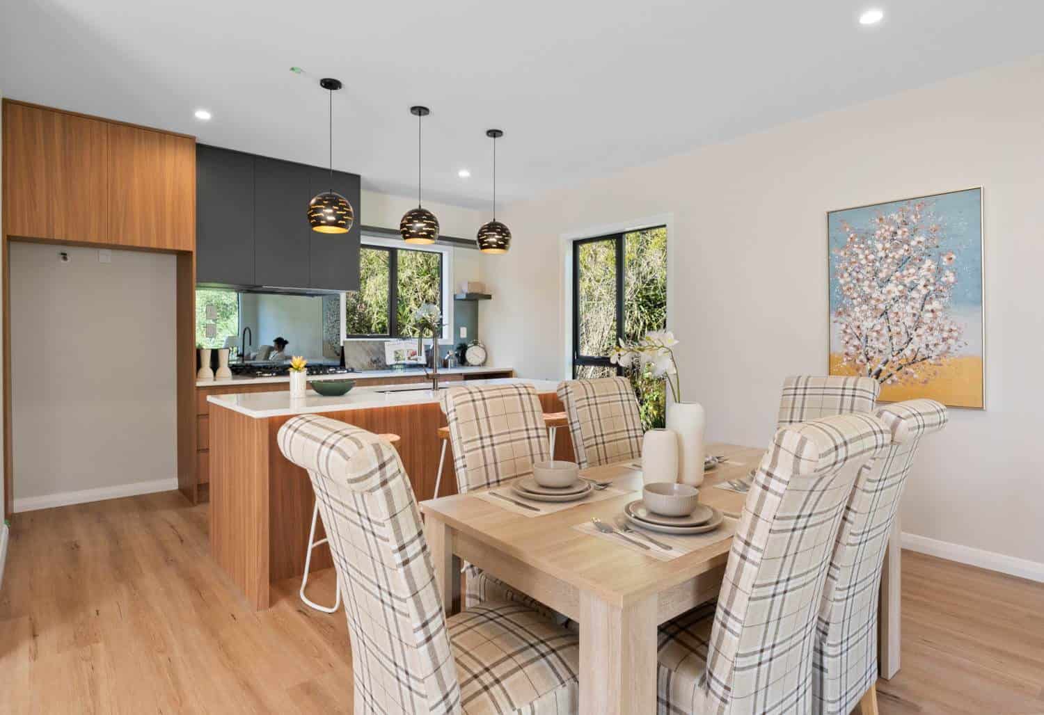 Dining table in front of a kitchen with timber cabinetry and pendant lights, Browns Bay