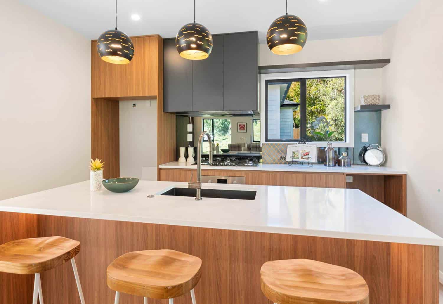 Kitchen island with timber stools, pendant lights and a dark splashback, Browns Bay