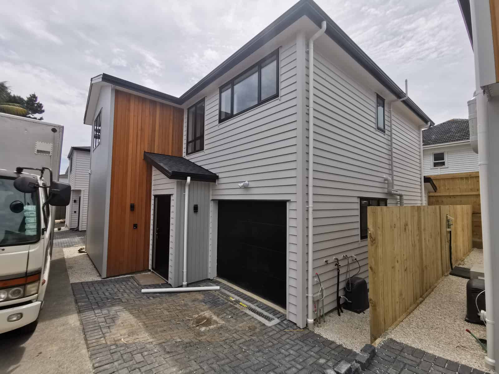 Side elevation of a new house with a timber-clad stair core beside the boundary fence, Blockhouse Bay