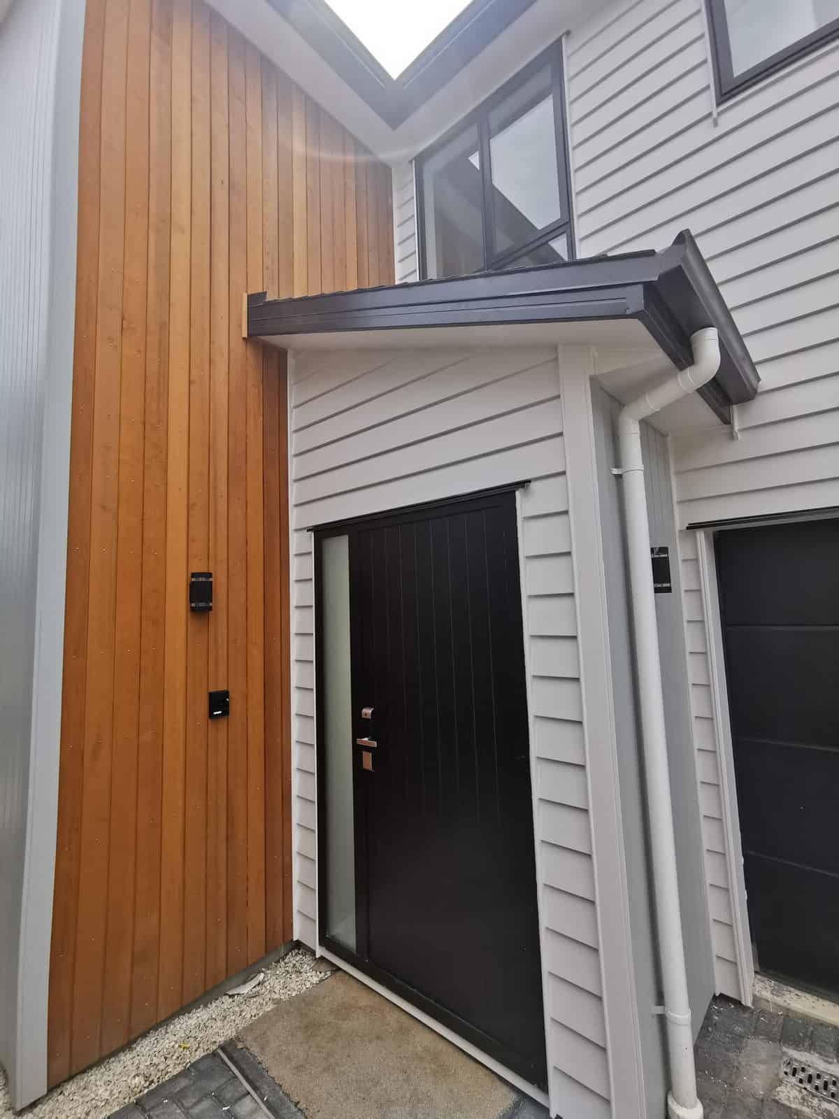 Front entry with a black door set against timber and weatherboard cladding, Blockhouse Bay