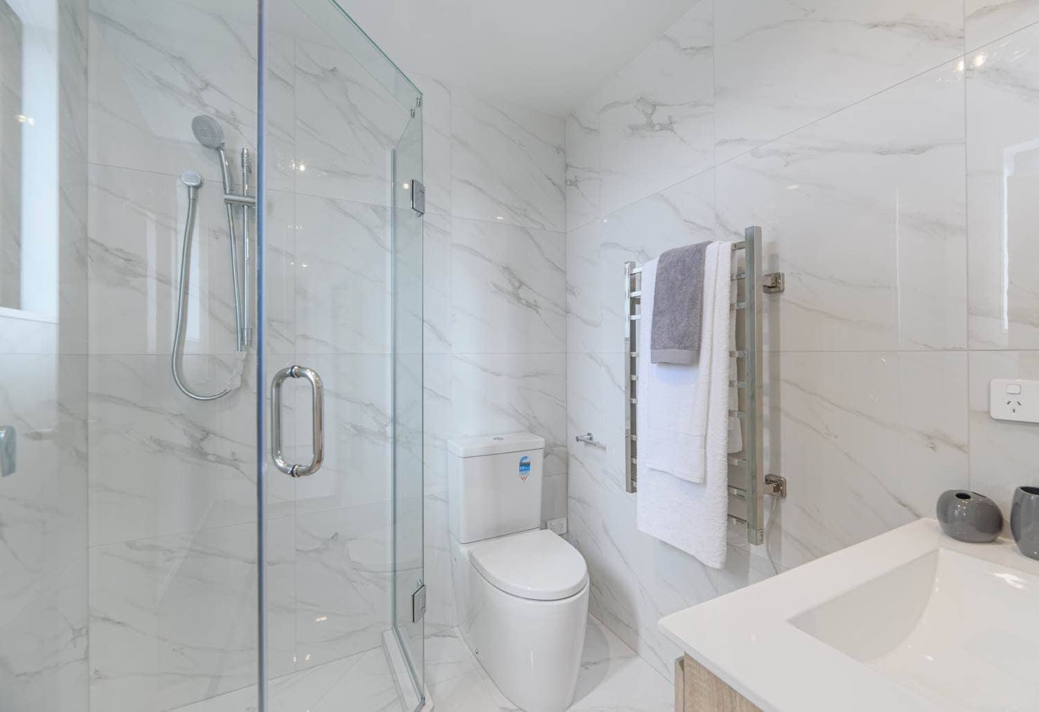 Bathroom with a corner glass shower, wall-hung toilet and marble-look tiling, Blockhouse Bay