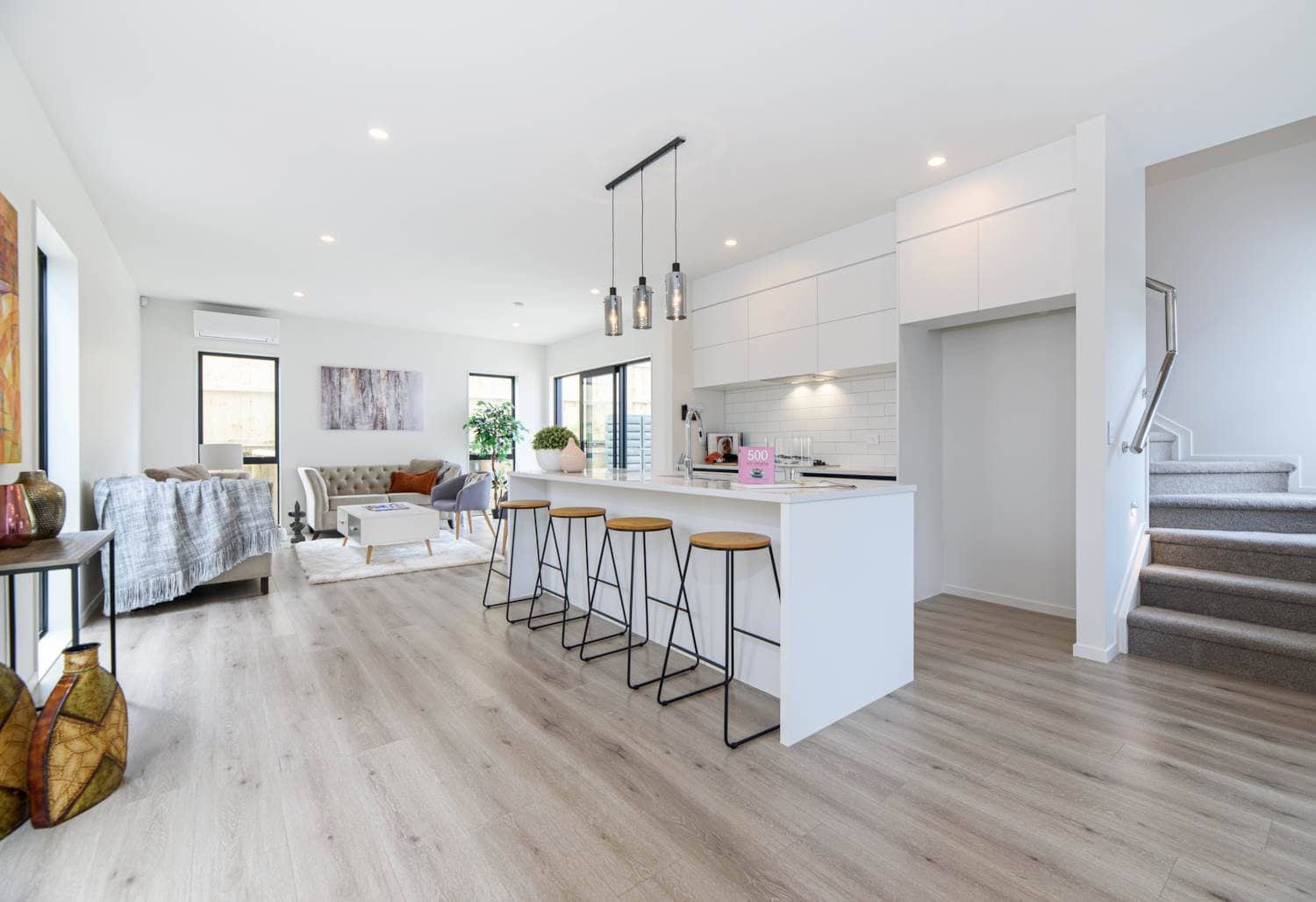 Open-plan living and kitchen with an island and bar stools beside the stair, Blockhouse Bay