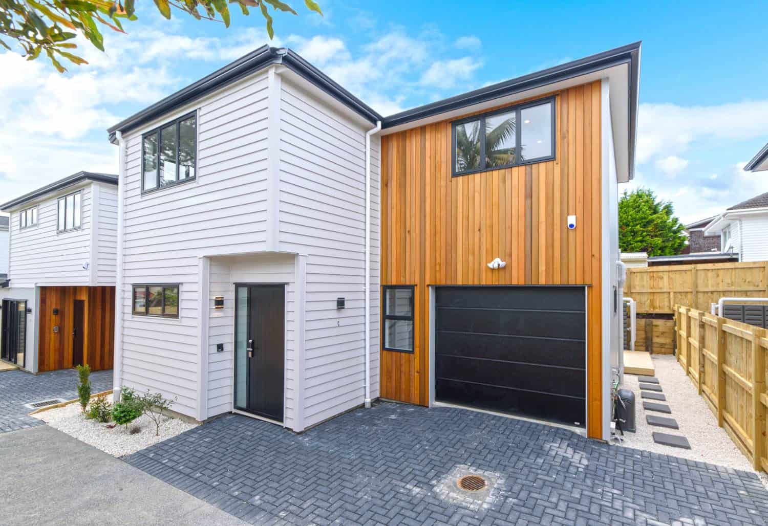 Two-storey house in white weatherboard and timber cladding with a paved driveway, Blockhouse Bay