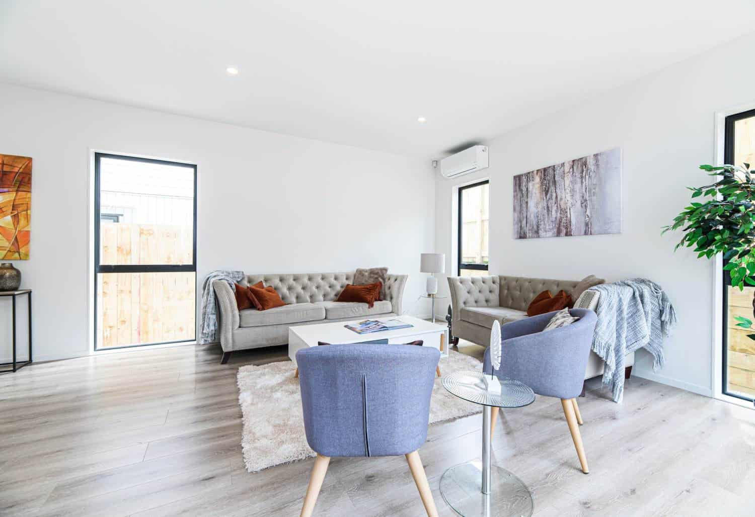 Living room with a sofa, armchairs and a wall-mounted heat pump, Blockhouse Bay