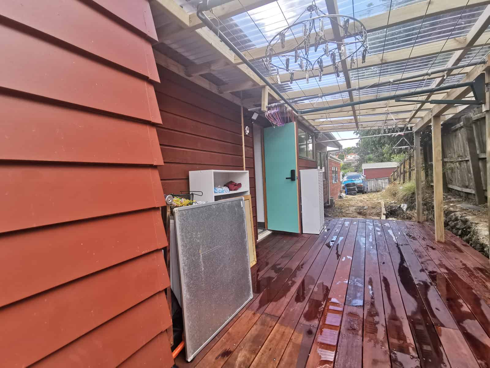 Covered timber deck beside the red-clad wall under a polycarbonate roof, Botany Downs