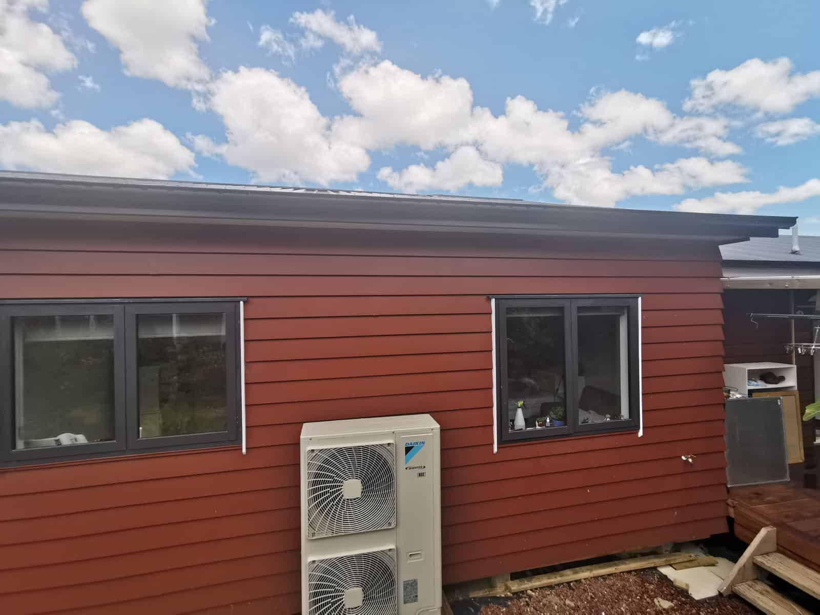 Red-clad elevation with two windows and an outdoor heat pump unit, Botany Downs