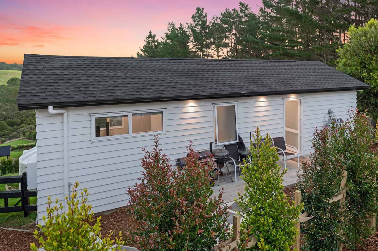 Side of the minor dwelling with new planting and a deck at dusk, Coatesville