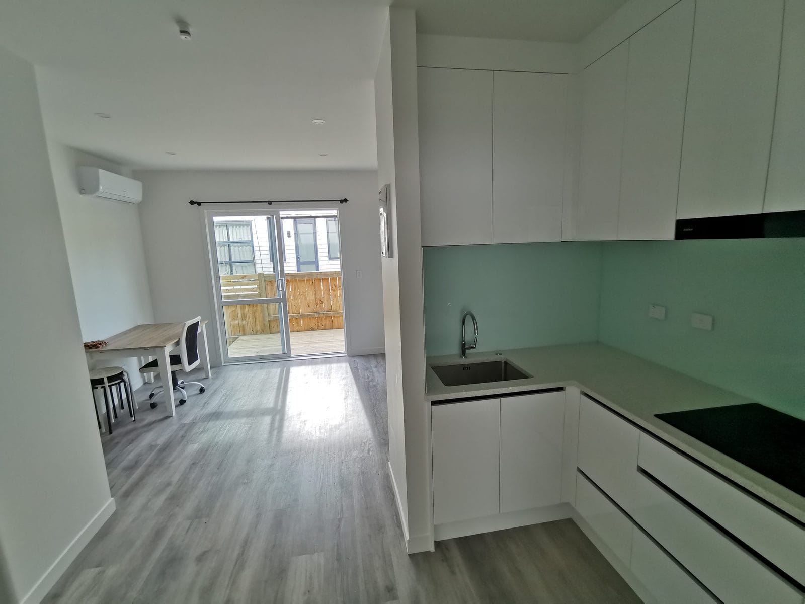 Kitchen with white cabinetry and a mint glass splashback looking to the deck, Albany
