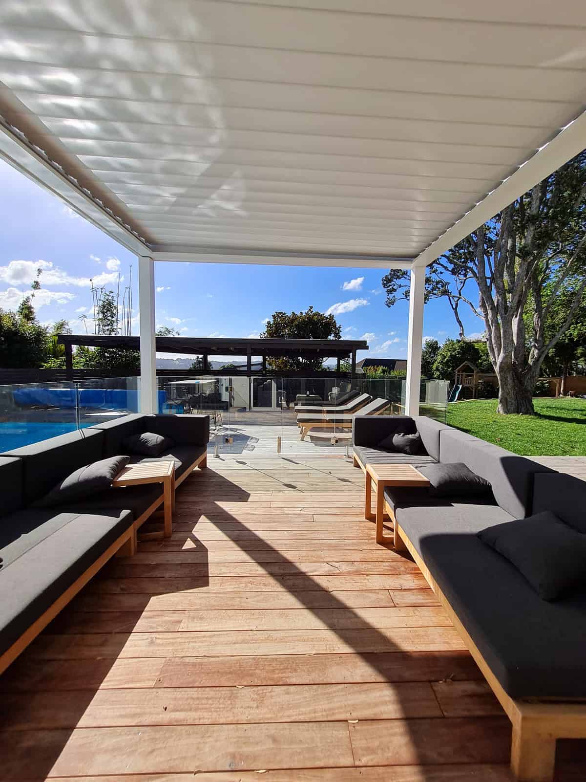 Louvre-roofed pool shelter with built-in seating looking down the deck to the pool, Greenhithe