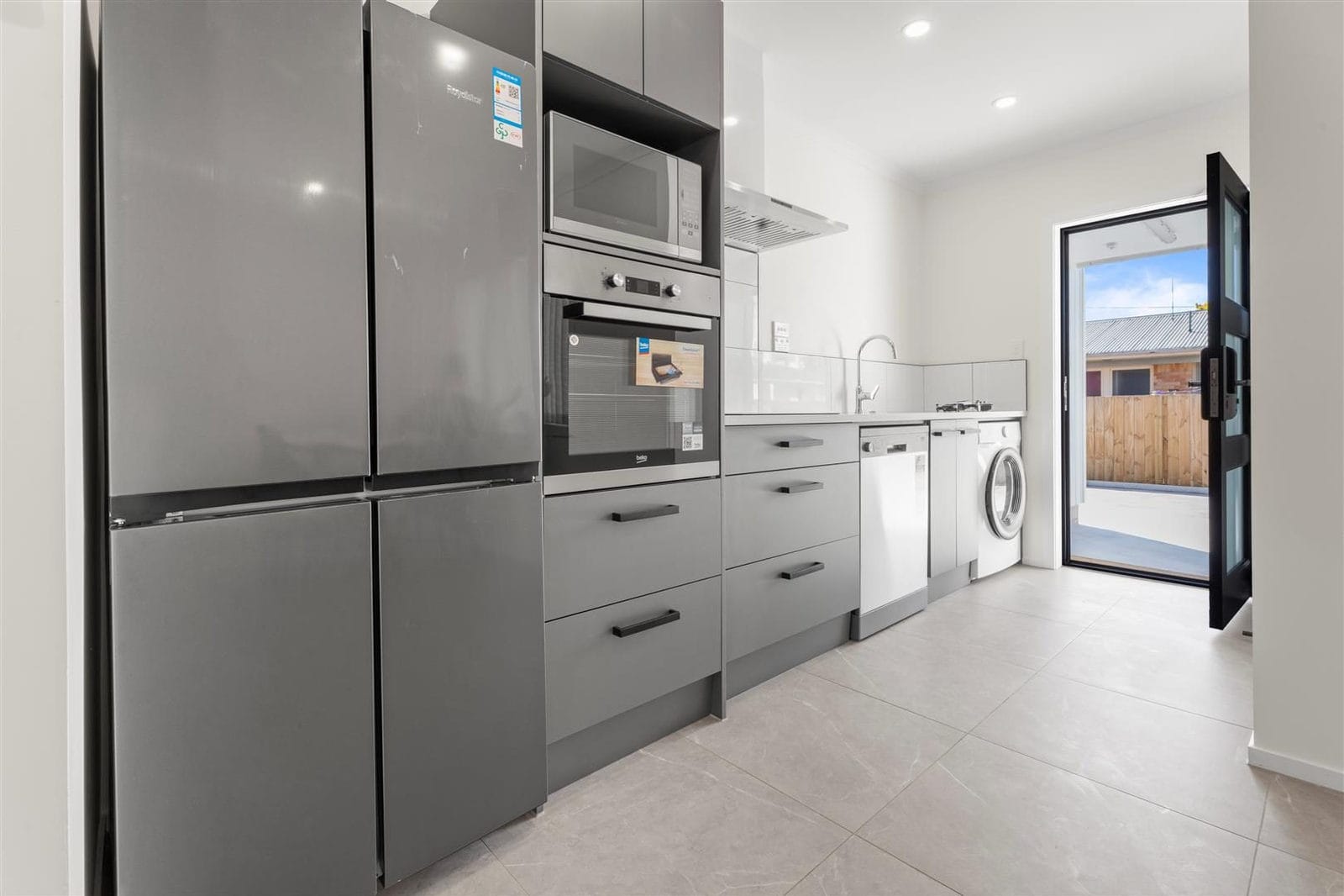 Galley kitchen with a large fridge, wall oven and laundry appliances beyond, Hamilton