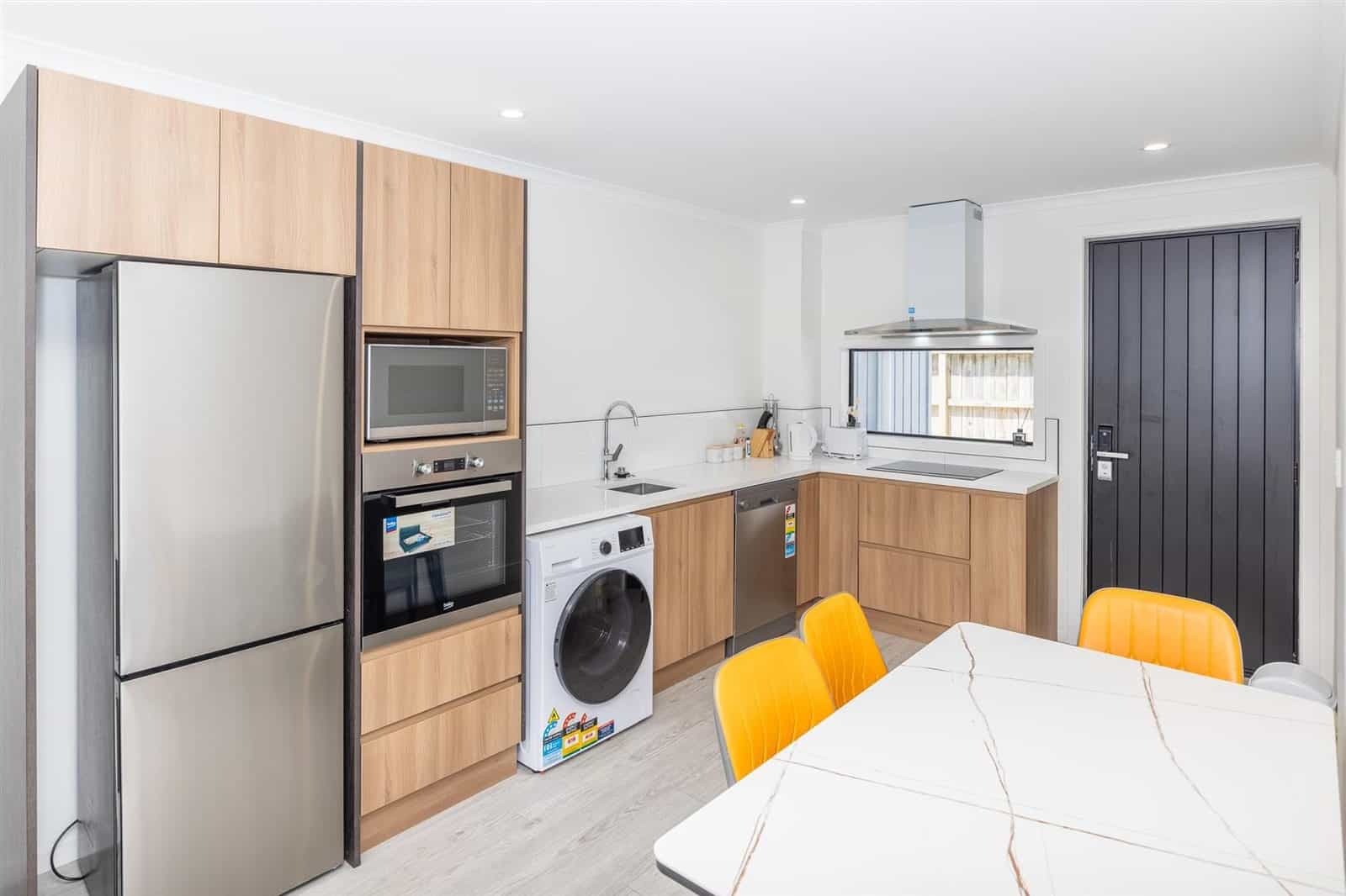 Kitchen with timber cabinetry, fridge, wall oven and washing machine beside the dining table, Hamilton