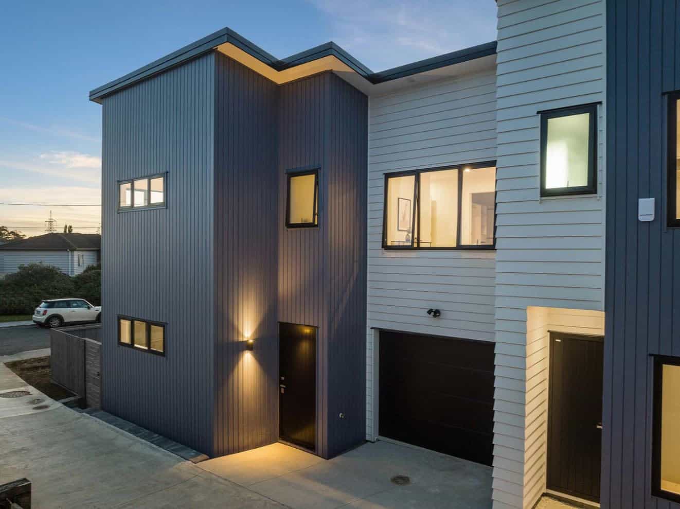 Two-storey house in blue and grey cladding lit at dusk with an integrated garage, Lynfield