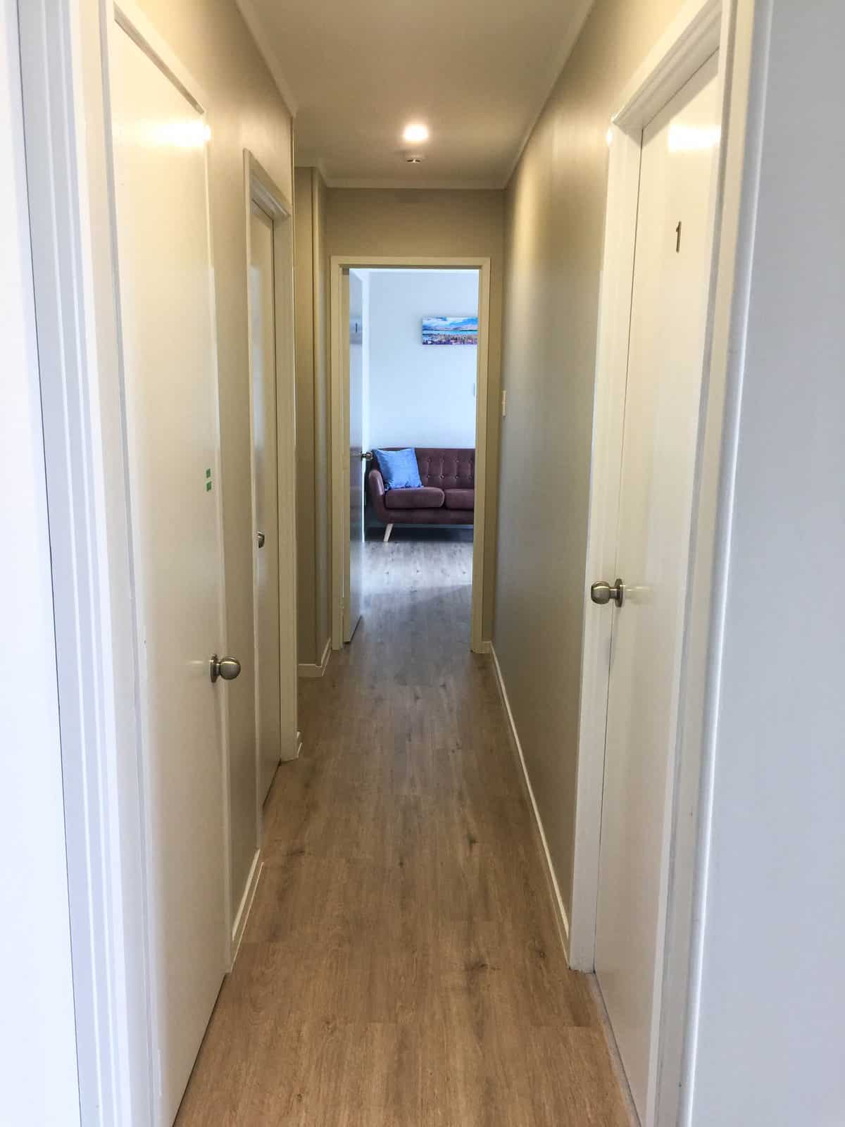 Existing hallway with timber-look flooring looking through to a bedroom, Mairangi Bay