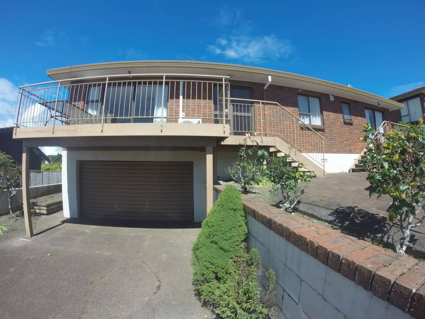 Existing two-storey brick house with a curved upper balcony and double garage, Mairangi Bay