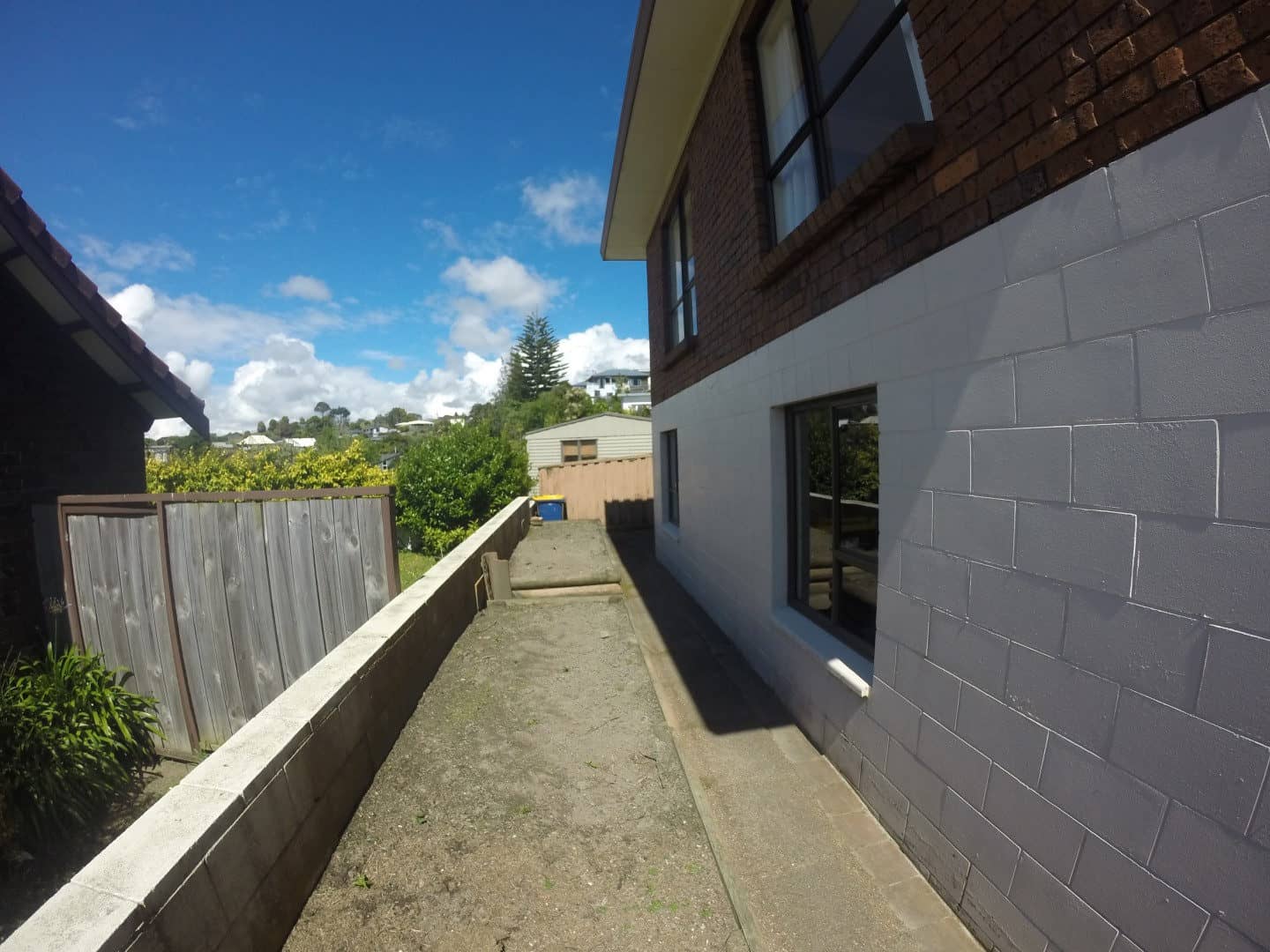 Narrow side passage between the rendered block wall and the boundary fence, Mairangi Bay