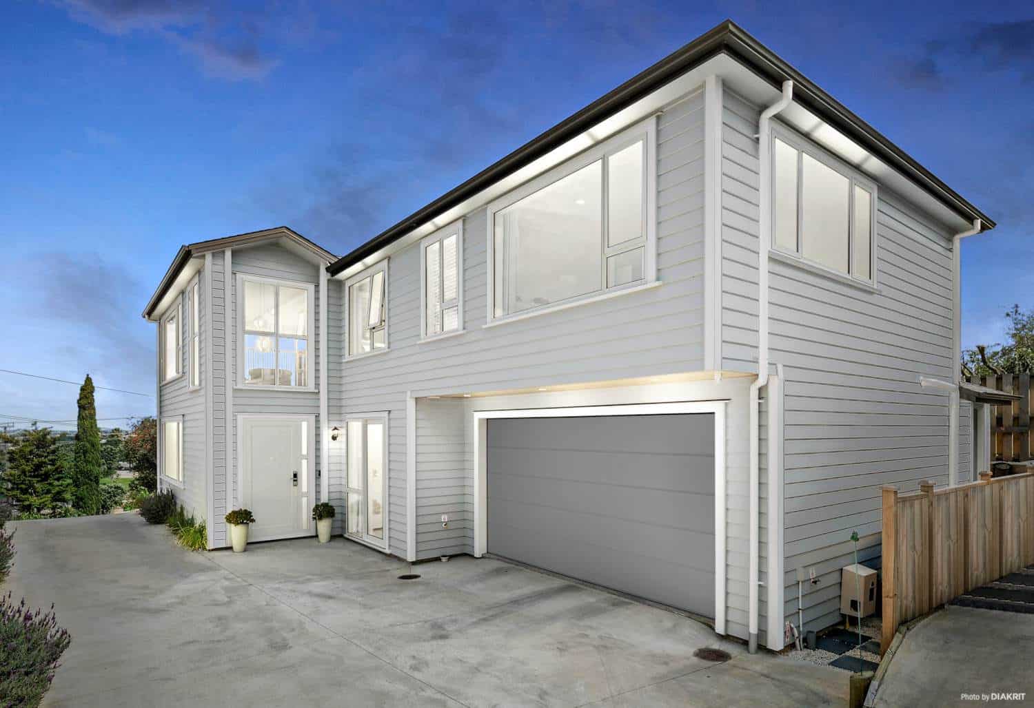Two-storey weatherboard house with a double garage and paved drive, Mairangi Bay