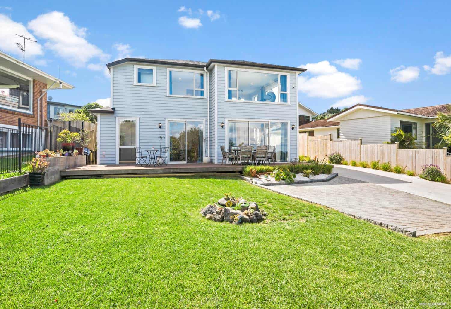 Rear of the house across the lawn with a paved terrace and new planting, Mairangi Bay