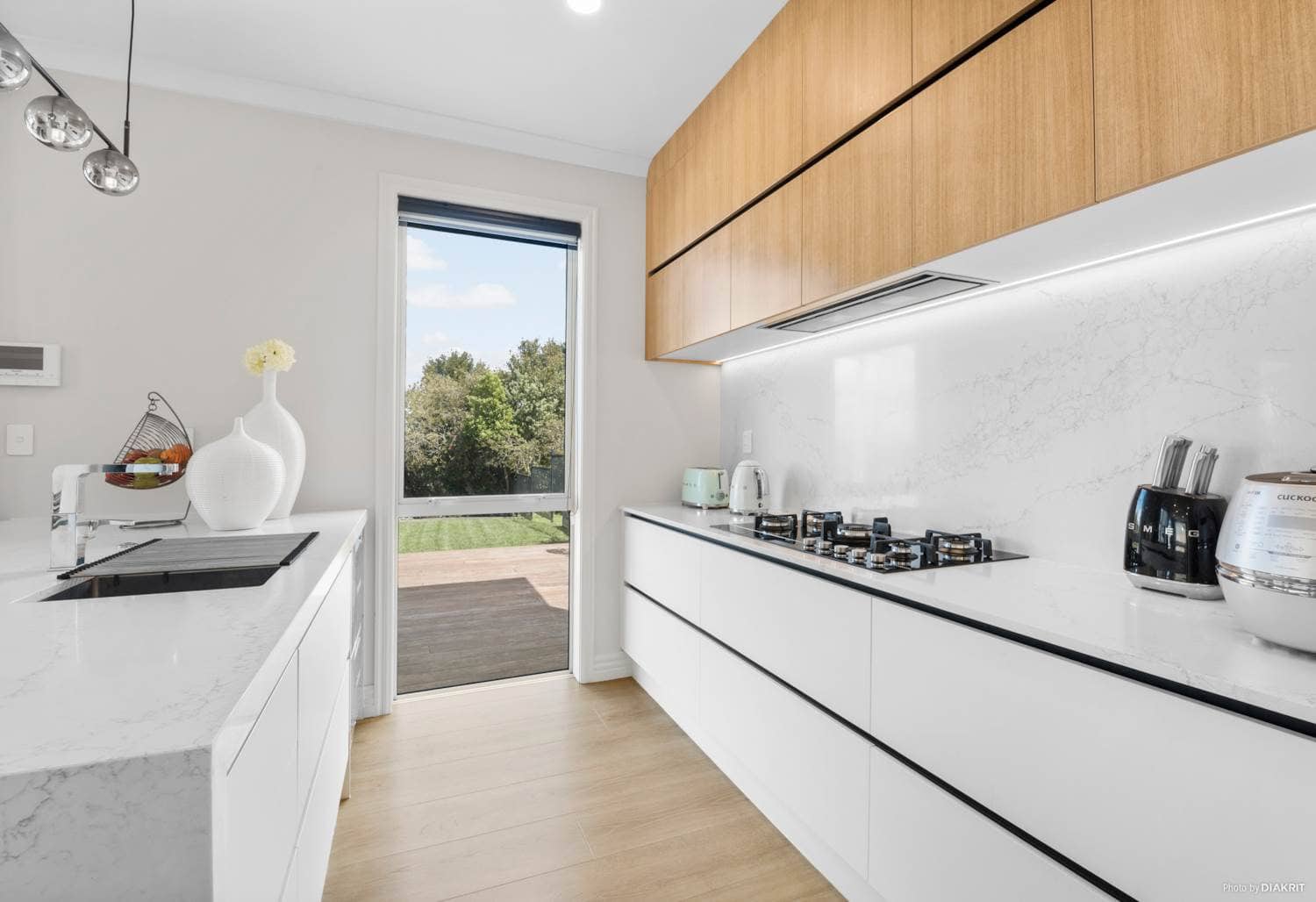 Kitchen with a white island, gas hob and timber overhead cabinetry, Mairangi Bay