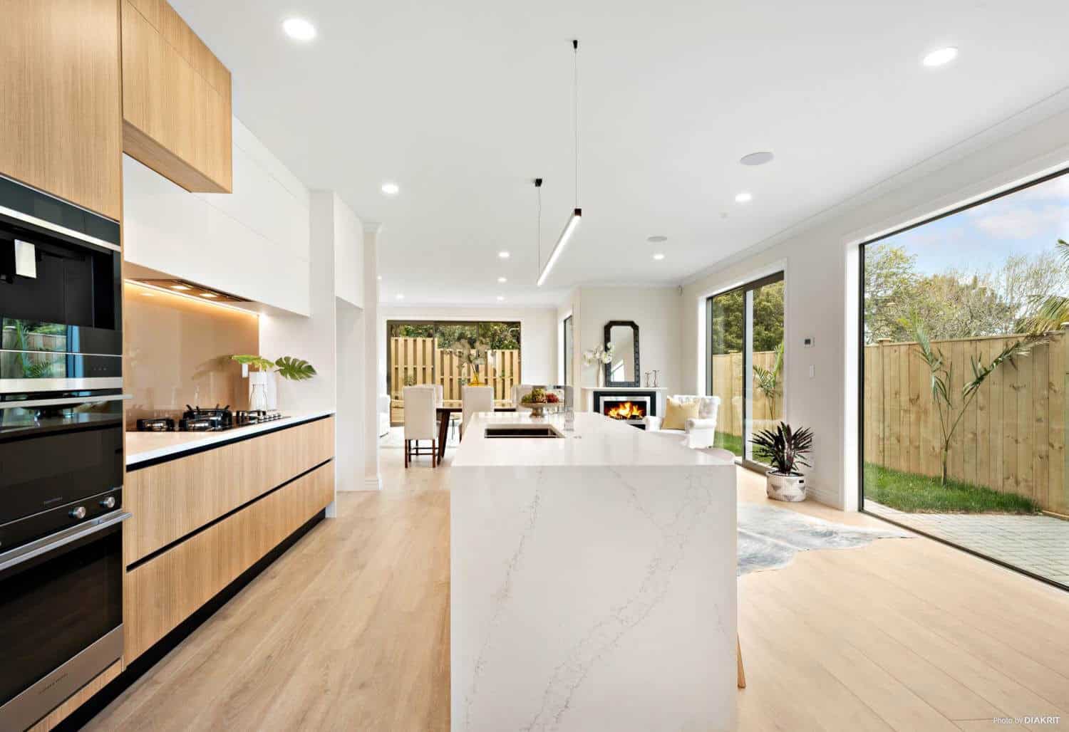 Kitchen with a stone island, wall ovens and timber overhead cabinetry, Mairangi Bay