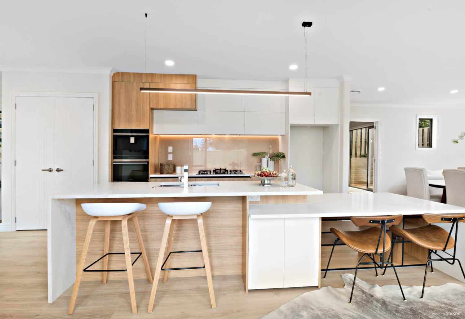 Kitchen with a white island, timber overhead cabinetry and bar stools, Mairangi Bay