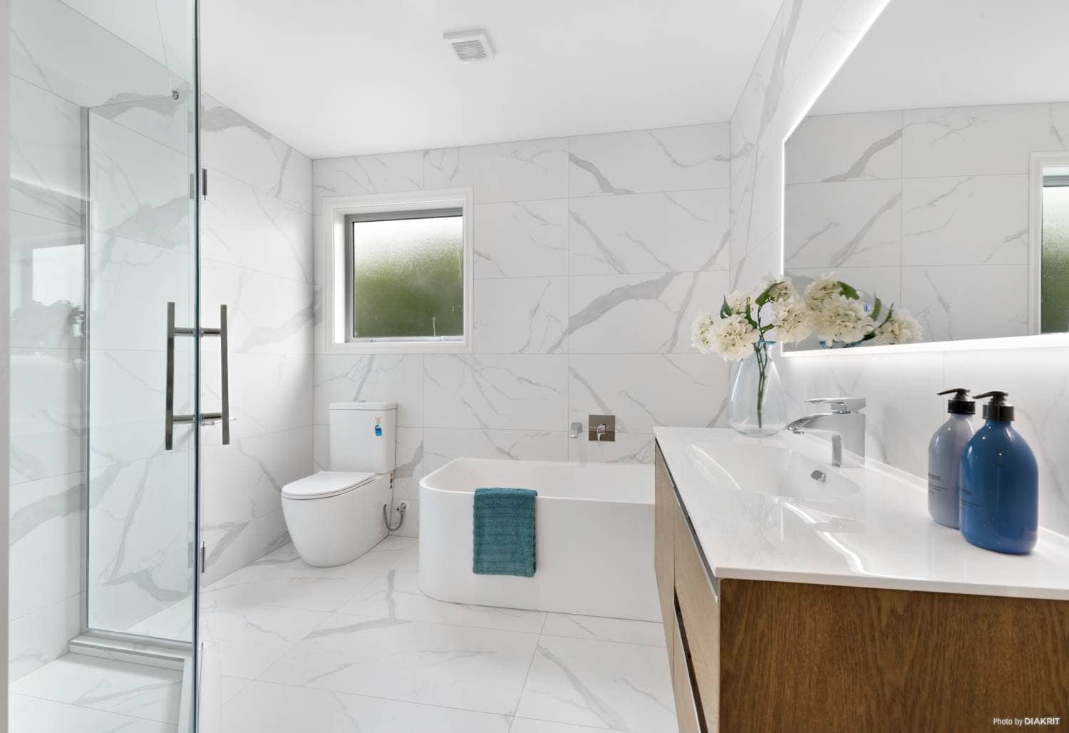 Bathroom with a bath, wall-hung toilet, timber vanity and marble-look tiling, Mairangi Bay
