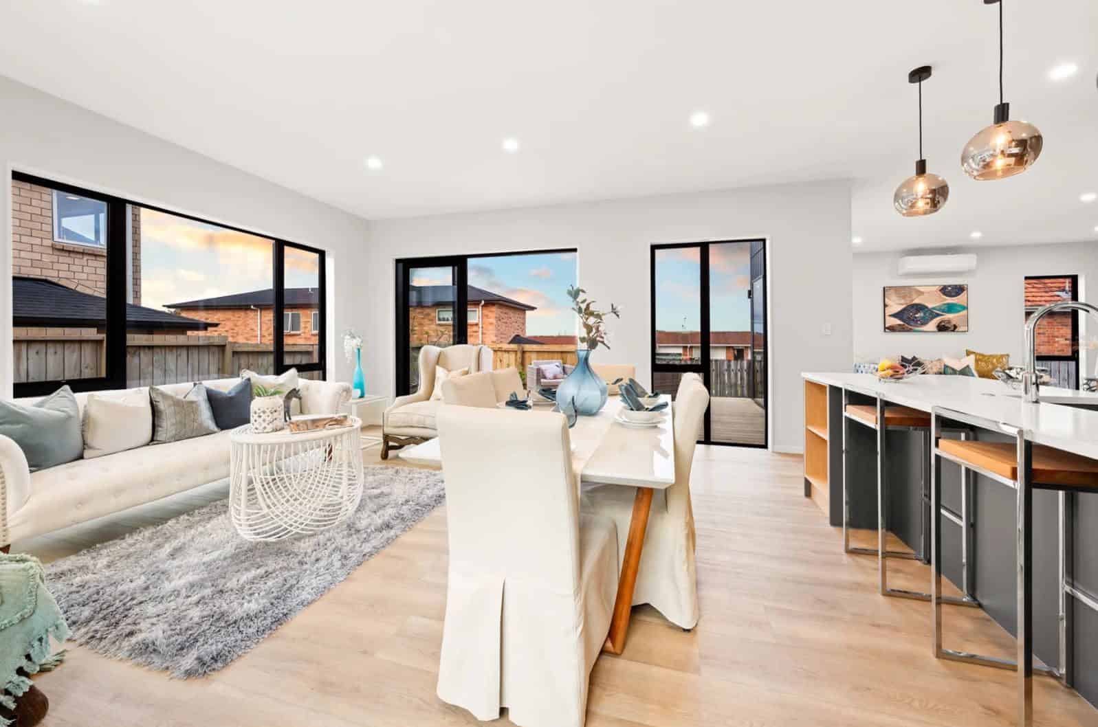 Living and dining with a grey kitchen island and pendant lights beyond, New Lynn