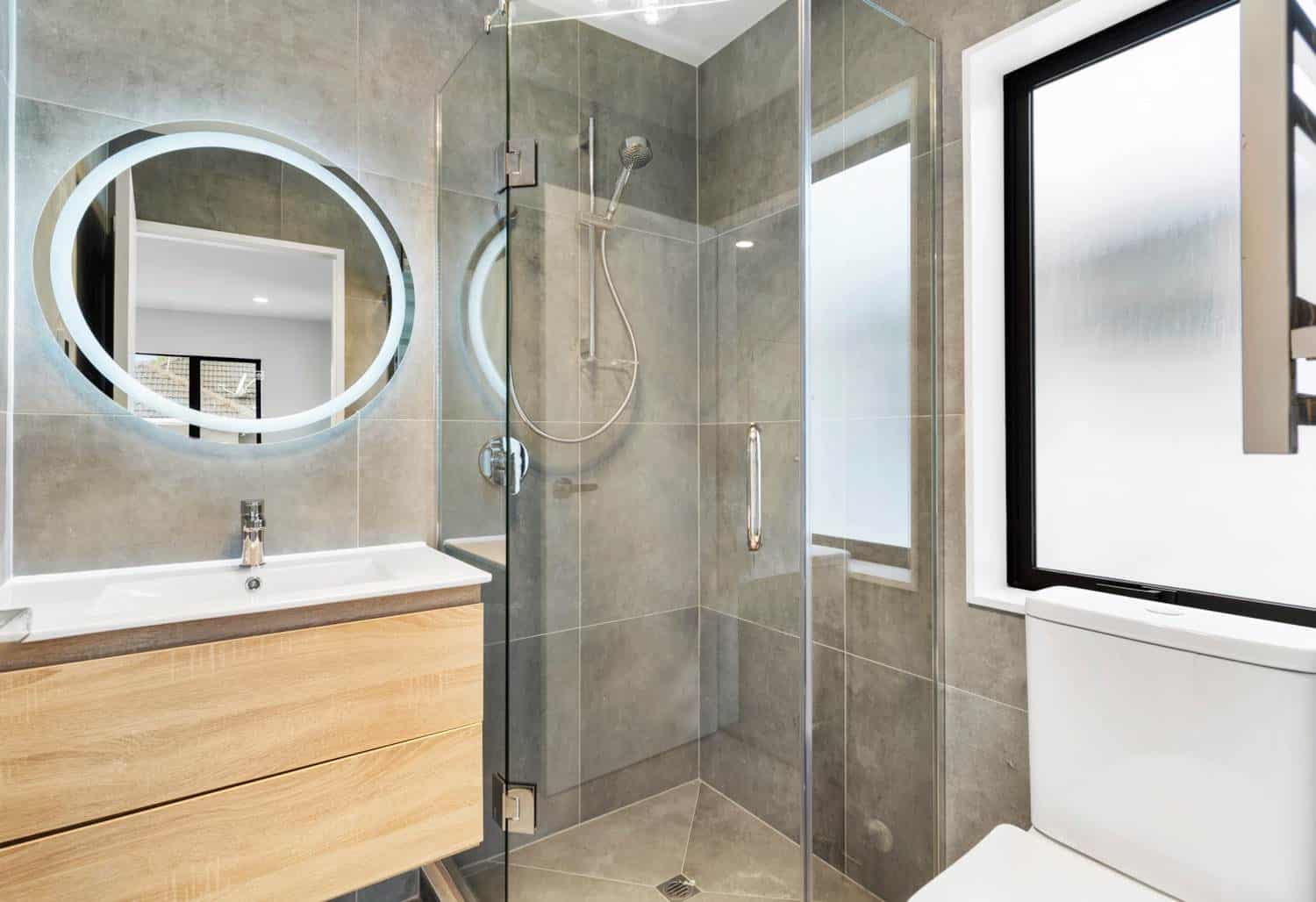 Bathroom with a backlit round mirror, timber vanity and glazed shower, New Lynn