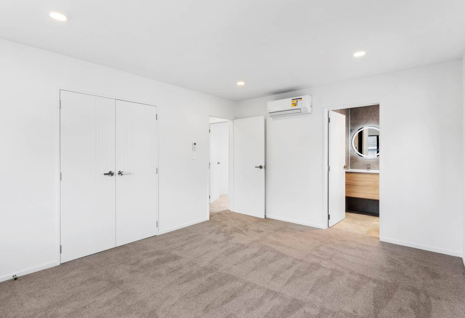 Empty bedroom with double wardrobe doors and an ensuite beyond, New Lynn