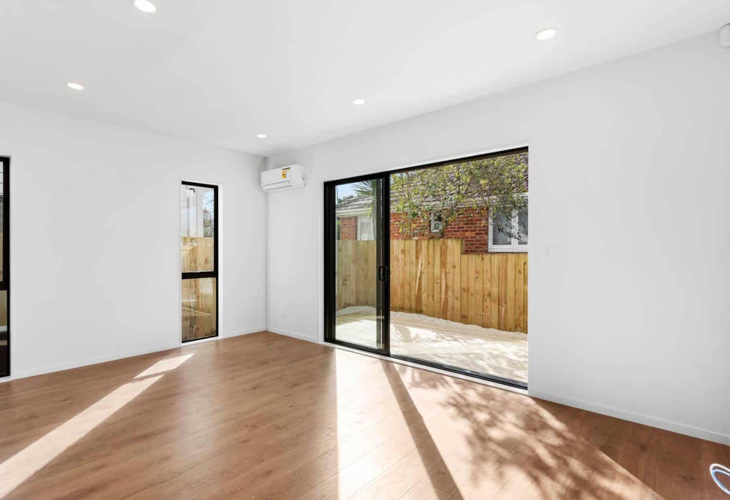 Empty living room with a sliding door onto a fenced courtyard, New Lynn