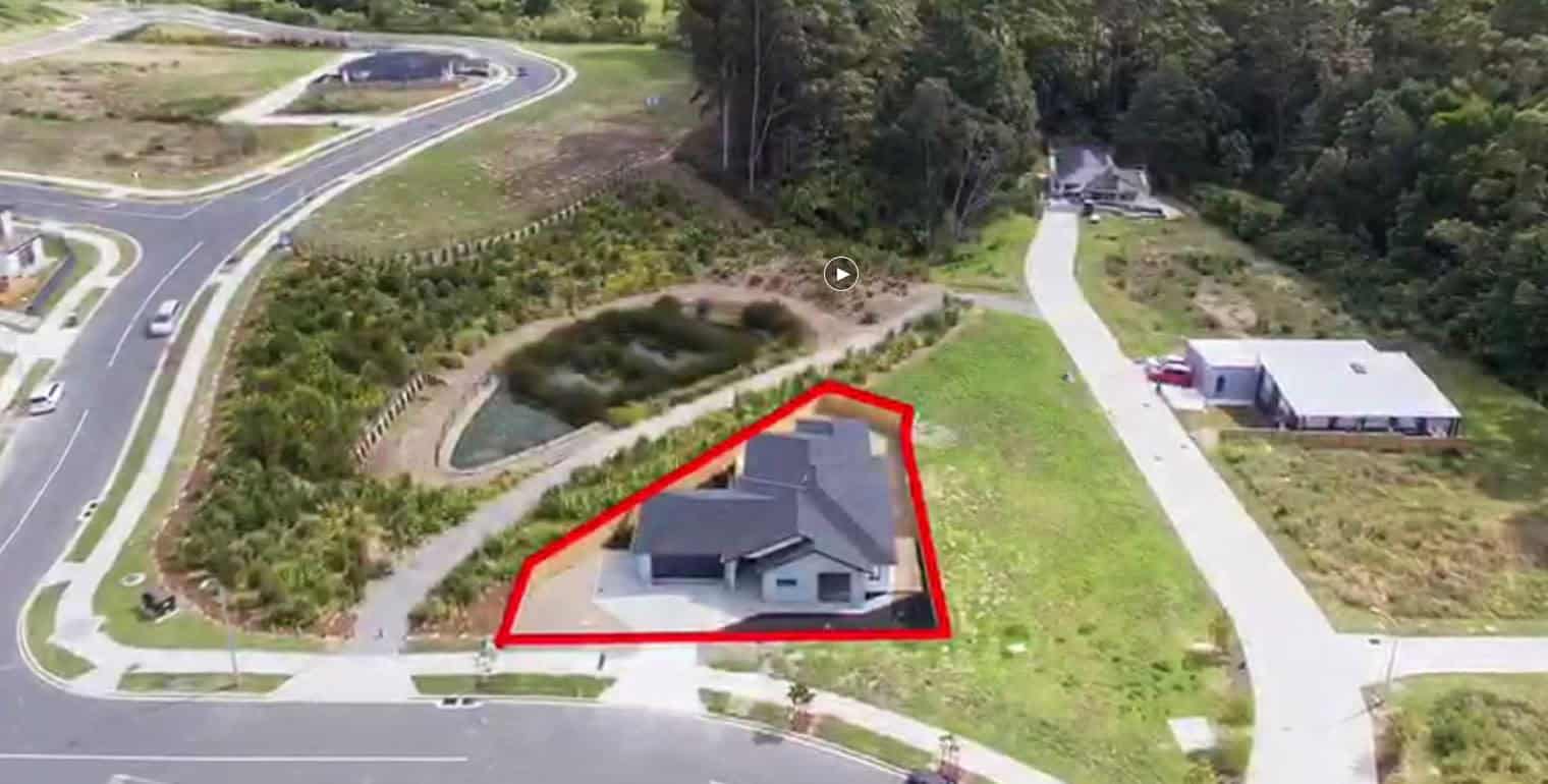 Aerial with the property outlined in red beside the road and a stormwater pond, Orewa