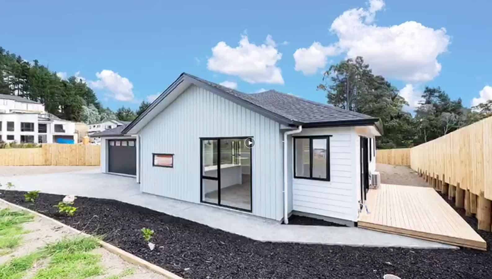 Side of a single-level house with a timber deck, new planting and a boundary fence, Orewa