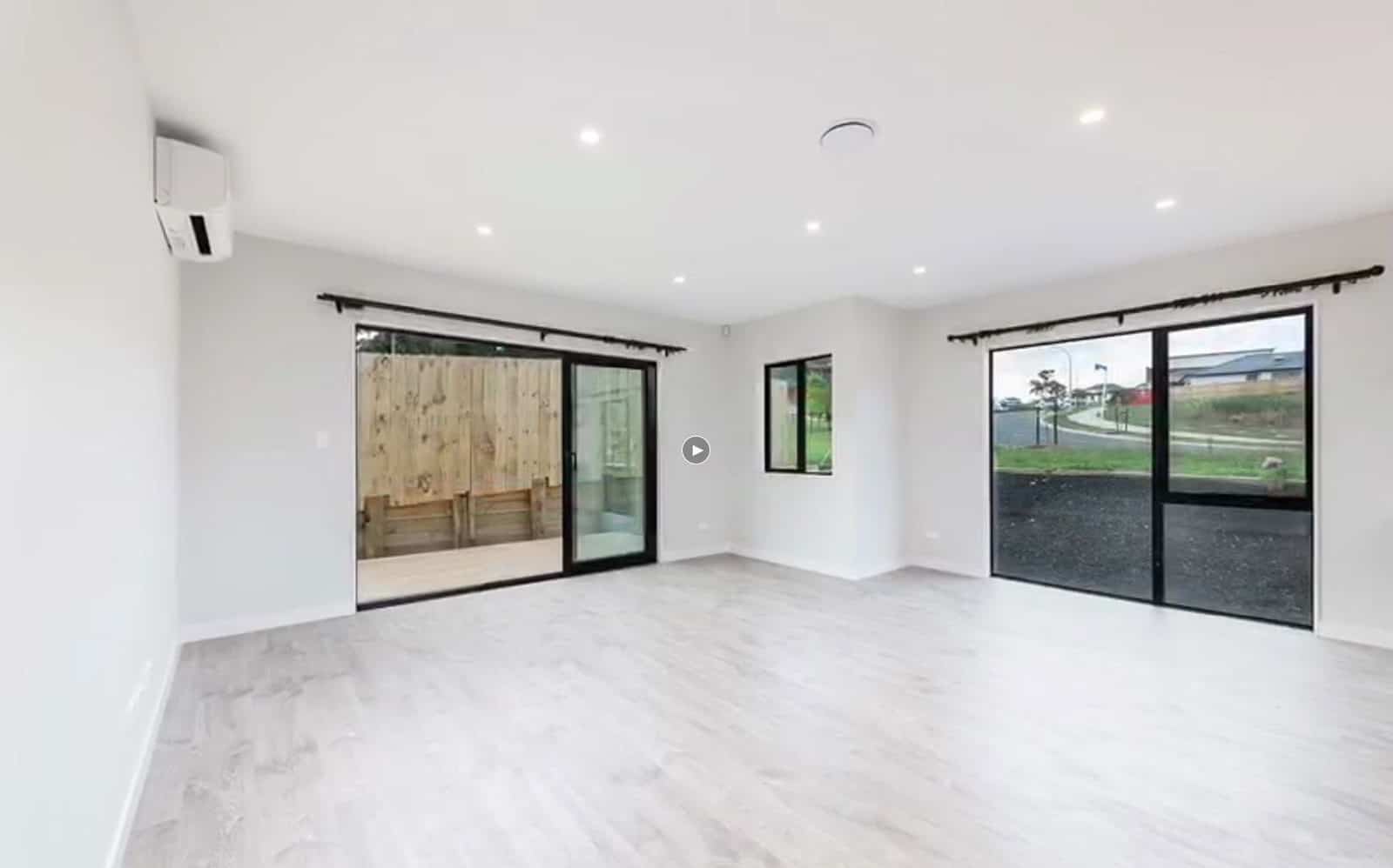 Empty open-plan living with sliding doors onto the deck and a heat pump, Orewa