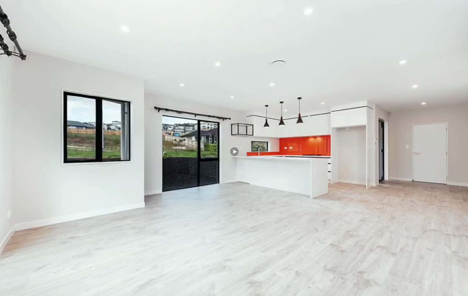 Empty living and dining looking through to the kitchen with its red splashback, Orewa