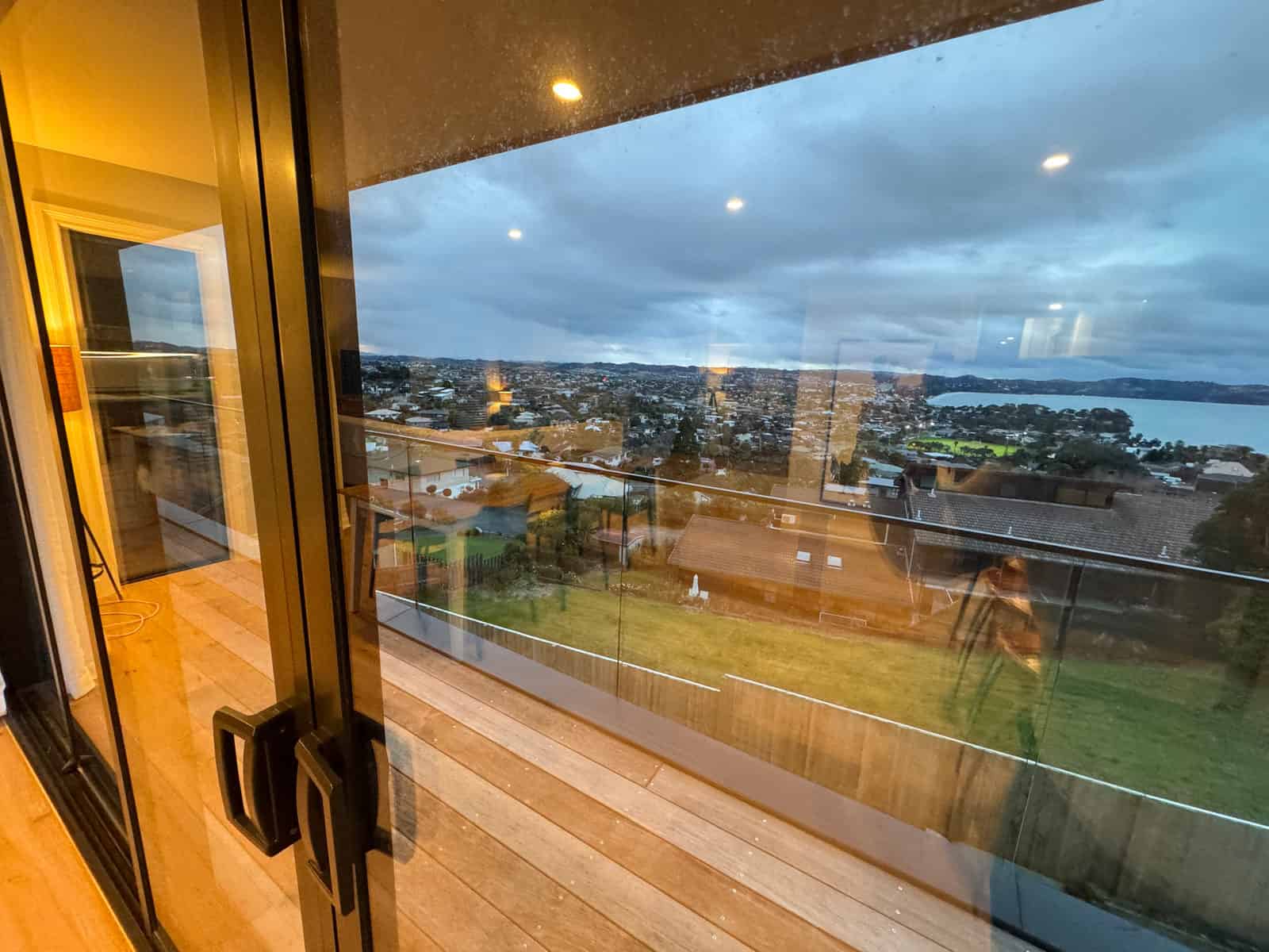 Sliding doors opening from a living room onto a deck with the estuary and coast beyond, Red Beach