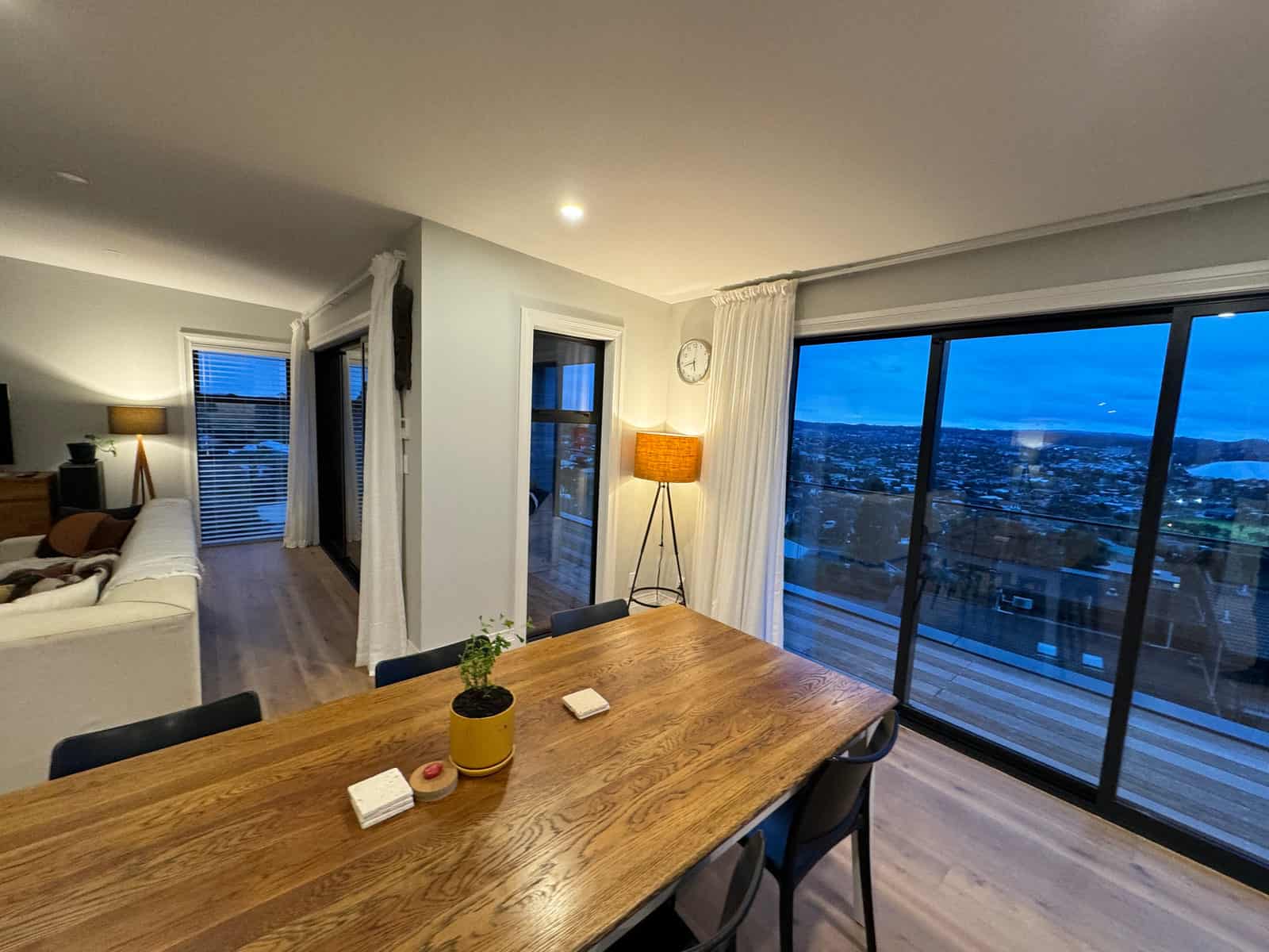 Dining table beside full-height glazing looking out over the estuary at dusk, Red Beach