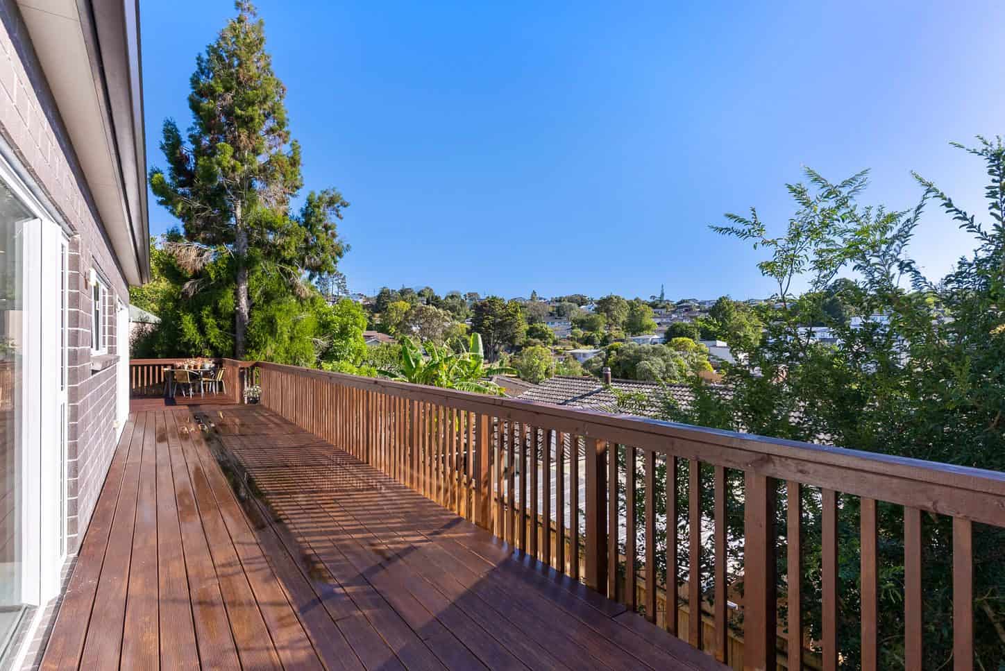 Timber deck running along the house with a view over trees to the suburb, Sunnynook