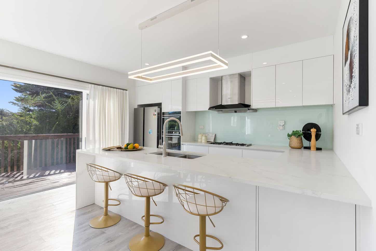 Kitchen with a stone island, mint glass splashback and gold bar stools, Sunnynook