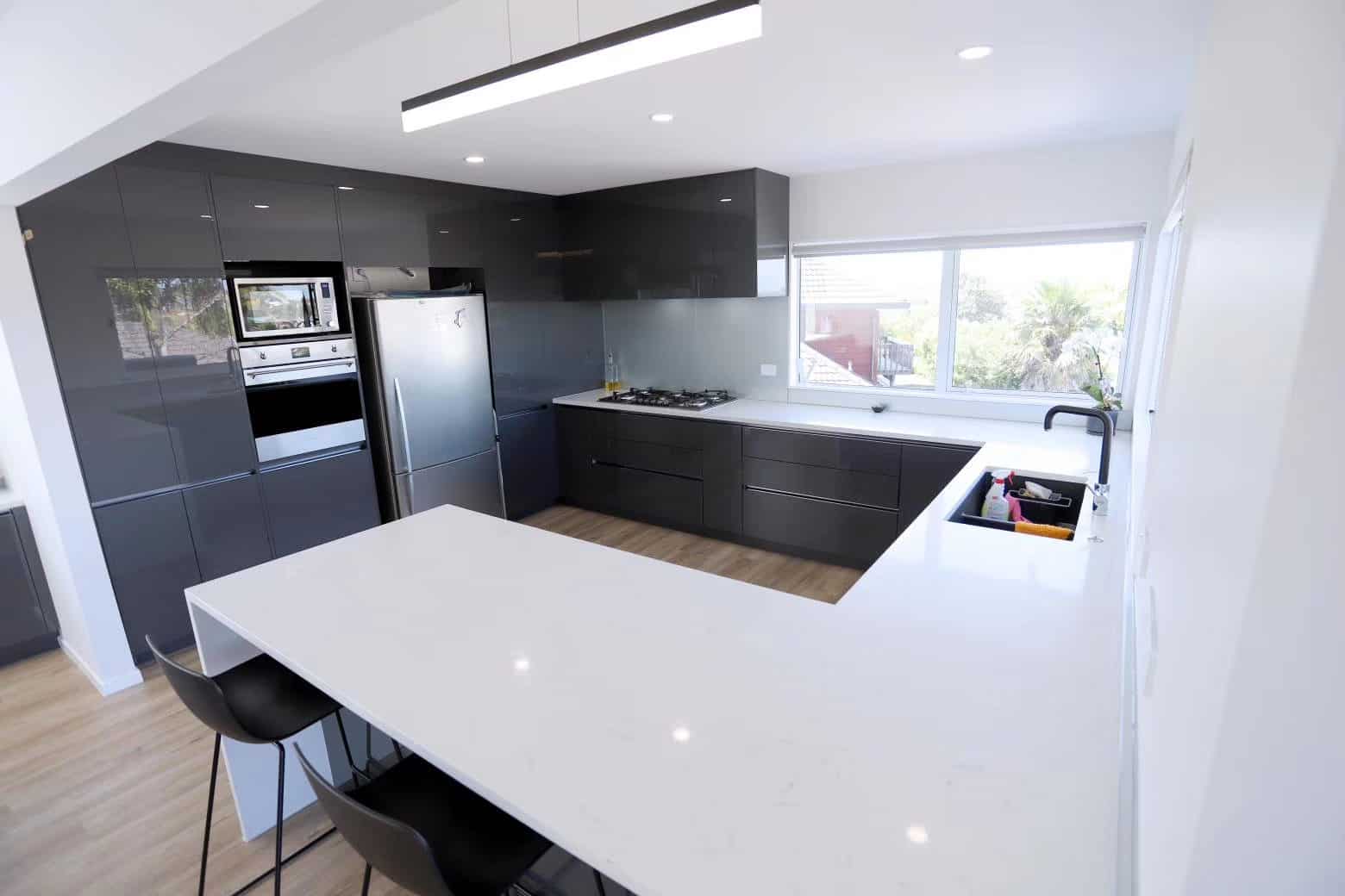 Open-plan kitchen with a white peninsula bench running into the dining area, West Harbour